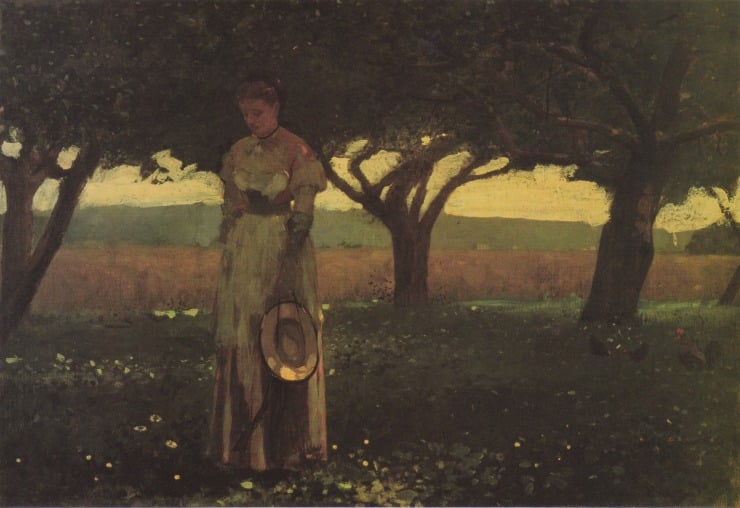 girl holds her hat underneath an orchard
